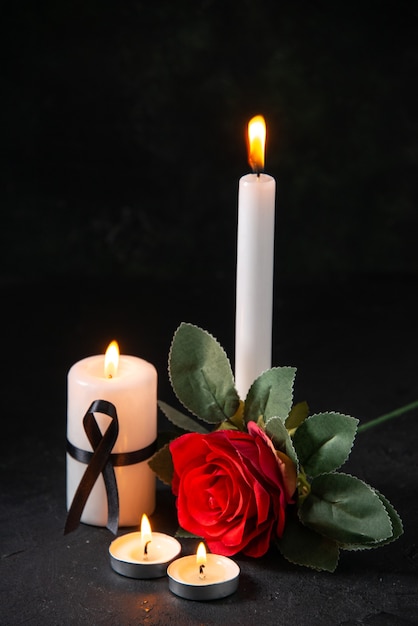 Vista frontal de uma vela acesa com uma flor vermelha na superfície escura