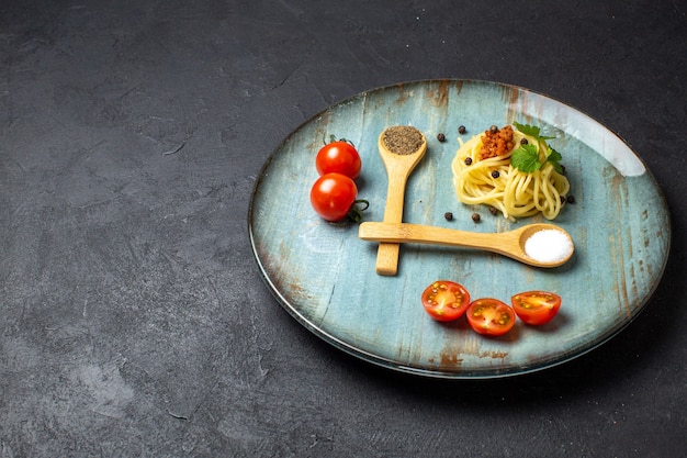 Vista frontal de la deliciosa comida de pasta servida con tomates de carne verde en un plato en el lado izquierdo sobre fondo negro