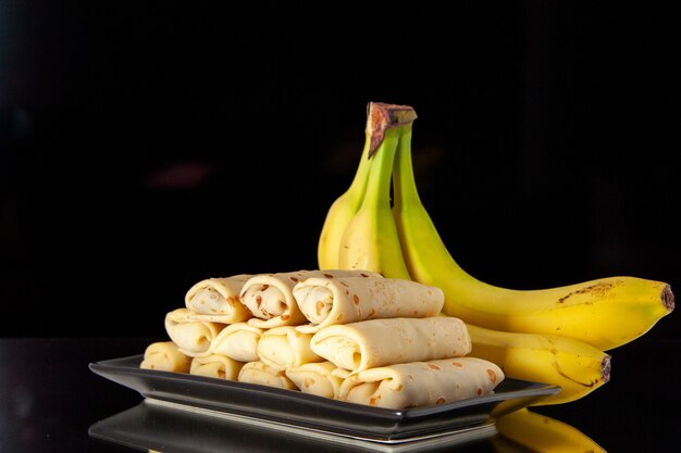 vista frontal deliciosas panquecas enroladas com bananas no fundo preto bolo doce manhã café da manhã açúcar sobremesa cor leite