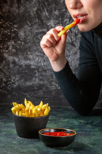 Vista frontal deliciosas papas fritas con condimentos que se comen por la superficie oscura femenina