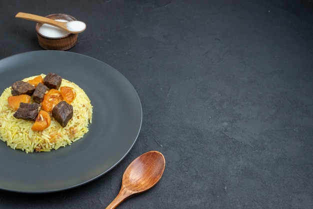 Vista frontal delicioso arroz cocido pilaf con rodajas de carne y condimentos sobre una superficie oscura