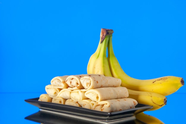 Foto vista frontal deliciosos panqueques enrollados con plátanos sobre fondo azul pastel dulce desayuno de la mañana postre de azúcar color leche