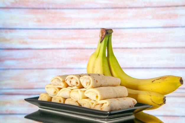 Foto vista frontal deliciosos panqueques enrollados con plátanos sobre fondo claro pastel de azúcar desayuno matutino postre leche de color