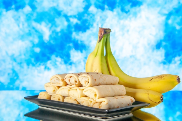 Foto vista frontal deliciosos panqueques enrollados con plátanos sobre fondo claro pastel de azúcar dulce mañana postre color leche