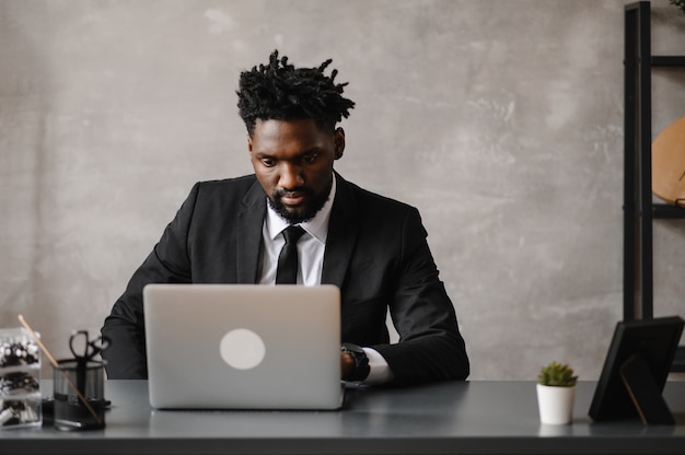 Vista frontal disparo a la cabeza joven empresario afroamericano sonriente mirando la pantalla del portátil