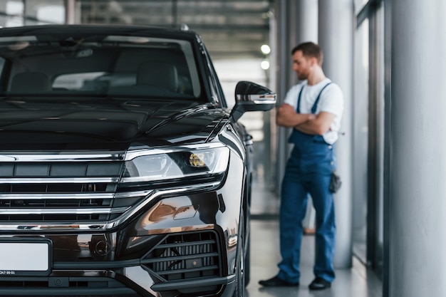 Vista frontal do carro Jovem de camisa branca e uniforme azul repara automóvel