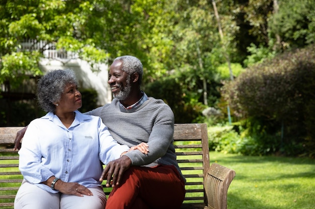 Vista frontal do casal afro-americano sênior no jardim, sentado em um banco, abraçando e conversando. Família aproveitando o tempo em casa, conceito de estilo de vida