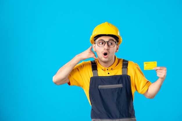 Vista frontal do construtor masculino de uniforme com cartão de crédito na parede azul