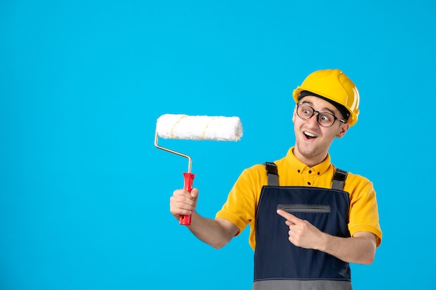 Vista frontal do construtor masculino de uniforme com o martelo nas mãos na parede azul