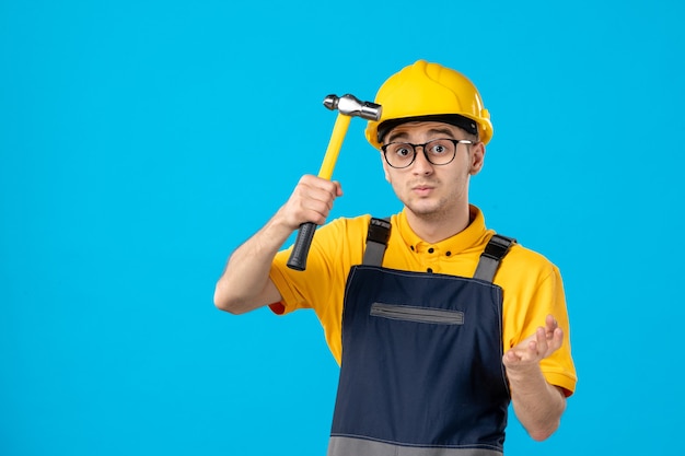 Vista frontal do construtor masculino de uniforme com o martelo nas mãos na superfície azul