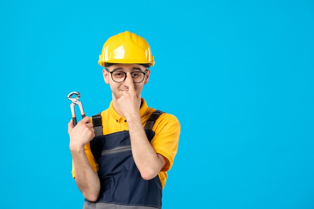 Vista frontal do construtor masculino de uniforme com um alicate na parede azul