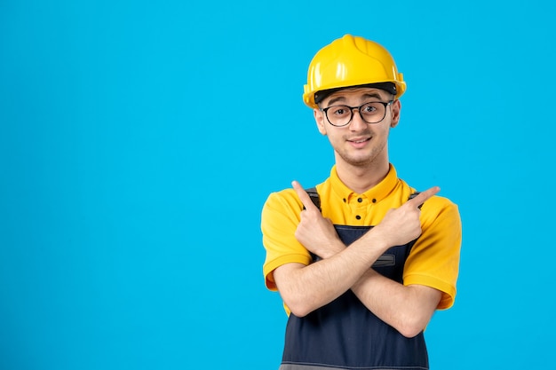 Vista frontal do construtor masculino de uniforme e capacete na superfície azul