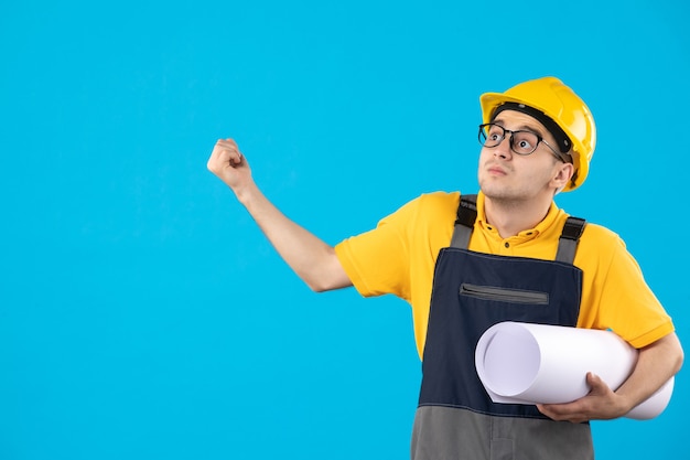 Vista frontal do construtor masculino em uniforme amarelo com plano de papel em azul