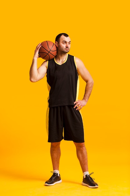 Vista frontal do jogador de basquete masculino, posando com a bola no ombro