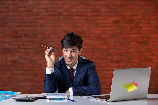 vista frontal do jovem empresário sentado atrás de seu local de trabalho em terno com avião de brinquedo plano de trabalho empreiteiro negócios trabalho construtor ocupação projeto corporativo