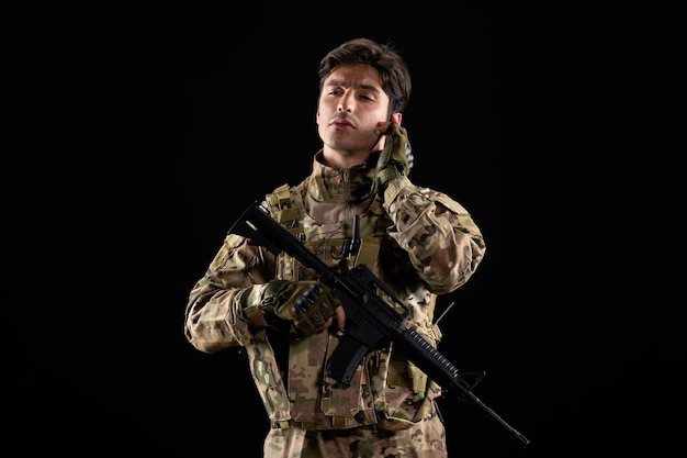 Vista frontal do jovem soldado de uniforme durante a operação na parede preta