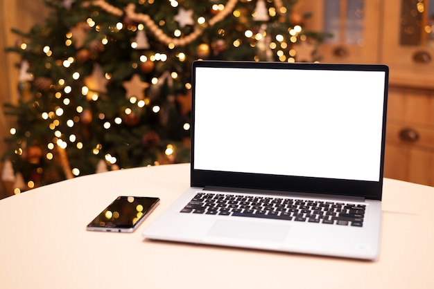 Vista frontal do laptop de tela branca em casa com luz quente da árvore de natal Trabalho remoto Teletrabalho