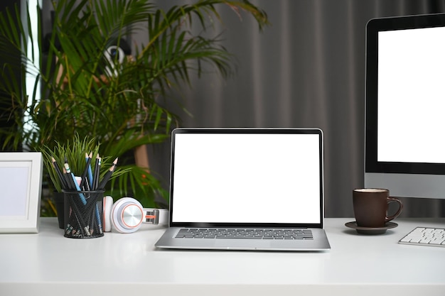 Vista frontal do laptop e computador com tela vazia na mesa branca no escritório em casa moderno