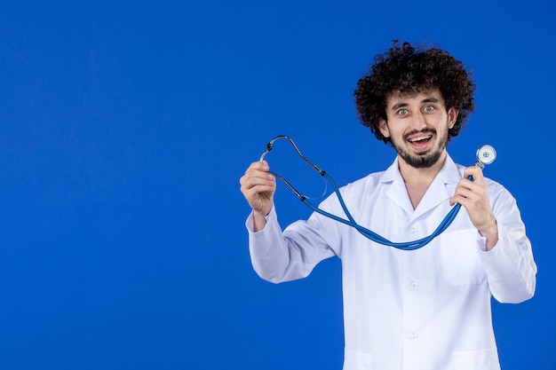 Vista frontal do médico masculino em traje médico segurando estetoscópio em fundo azul coronavírus saúde covid- vacina vírus hospital pandemia de drogas