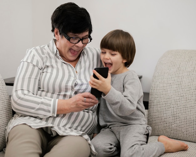 Foto vista frontal do neto sorridente e da avó olhando para o smartphone juntos