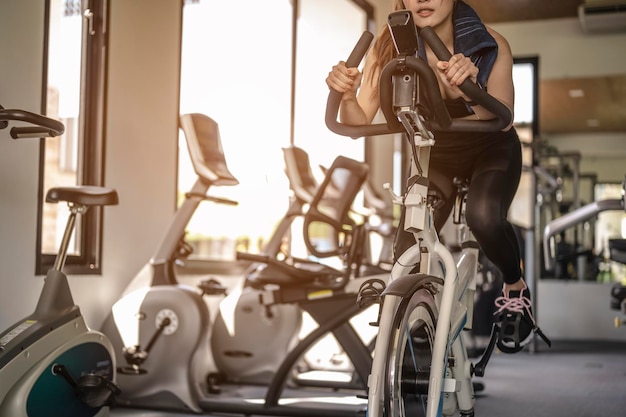 Foto vista frontal do treino de mulher com bicicleta. as mulheres se exercitam malhando na academia para um estilo de vida saudável na bicicleta ao pôr do sol. fitness, treino, ginástica, estilo de vida e conceito saudável.