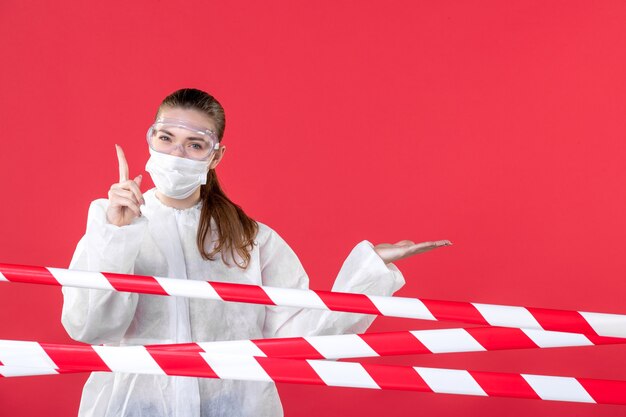 Vista frontal doctora detrás de tiras rojas-blancas selladas sobre fondo rojo línea de salud covid- cura aislamiento peligro virus hospital