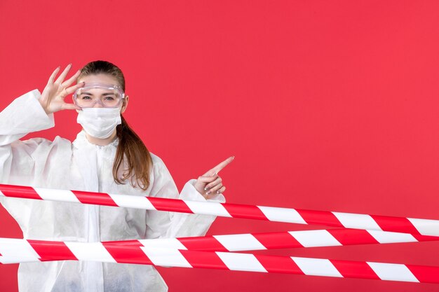 Vista frontal doctora detrás de tiras rojas-blancas selladas sobre el fondo rojo línea de salud hospital covid- cura aislamiento peligro virus
