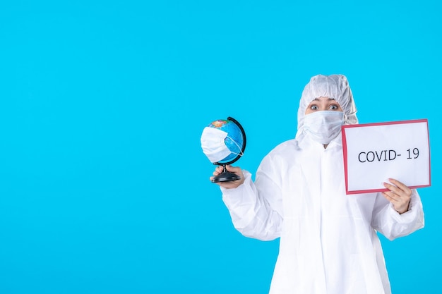 Vista frontal doctora en traje de protección y máscara sobre fondo azul covid- aislamiento de salud pandemia virus médico globe