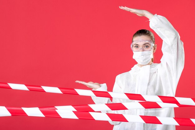 Foto vista frontal de la doctora en traje de protección y máscara sobre fondo rojo hospital emoción tejido covid- enfermera curar virus