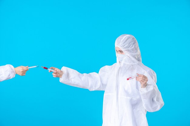 Vista frontal doctora en traje de protección y máscara sosteniendo la inyección sobre fondo azul ciencia del hospital médico covid- salud pandémica