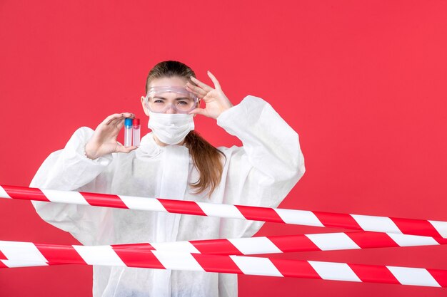 Vista frontal doctora en traje de protección sosteniendo frascos sobre el fondo rojo enfermera covid- cura de salud emoción máscara de virus tejido hospitalario