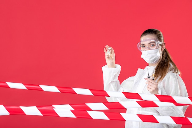 Foto vista frontal doctora en traje de protección sosteniendo inyecciones sobre fondo rojo enfermera covid- salud emoción máscara curar tejido virus