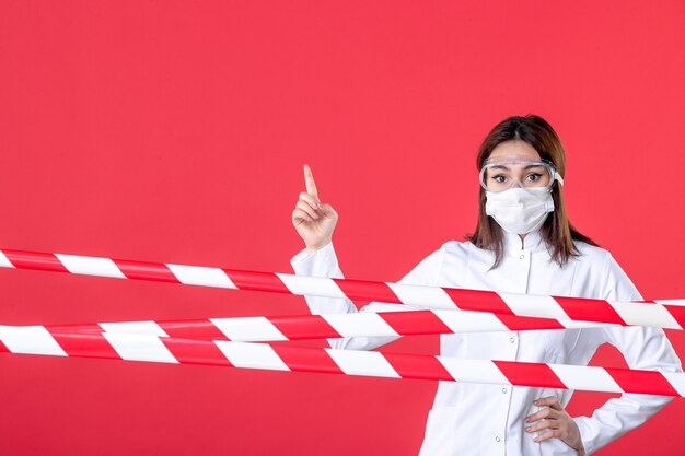 Vista frontal doctora en uniforme médico y máscara sobre un fondo rojo línea delictiva sellada virus covid- salud hospitalaria médica