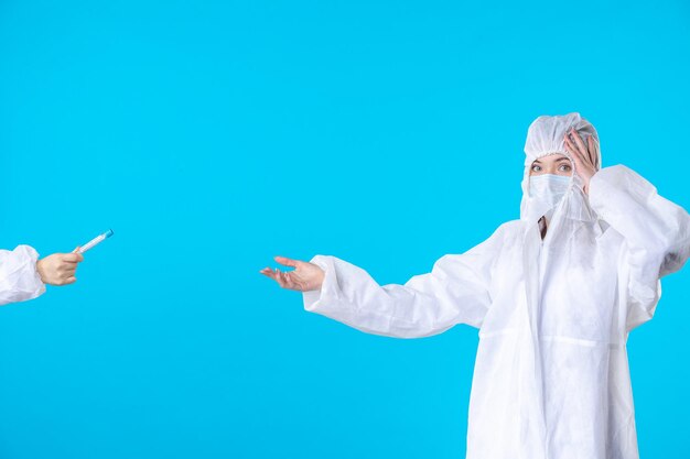 Vista frontal doctoras en trajes protectores y máscaras sosteniendo frascos sobre fondo azul salud del hospital médico covid-virus pandémico