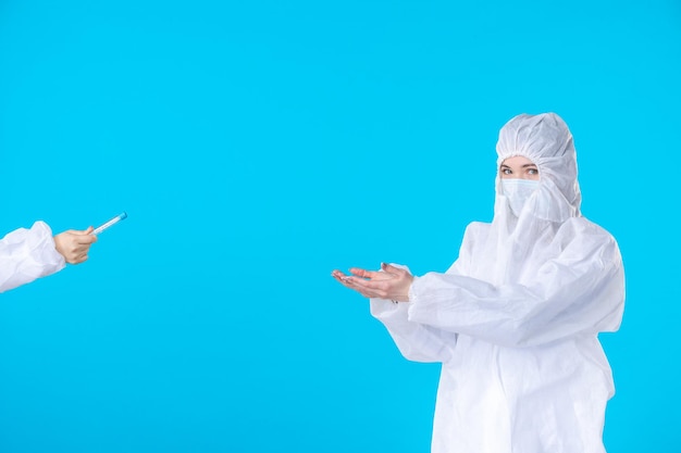 Vista frontal doctoras en trajes protectores y máscaras tomando matraz sobre el fondo azul hospital médico ciencia de la salud covid-virus pandémico