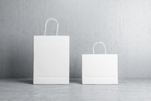 Vista frontal de dos bolsas de compras de papel blanco en blanco con lugar para su logotipo o texto en piso de concreto sobre fondo gris simulacro de representación 3d