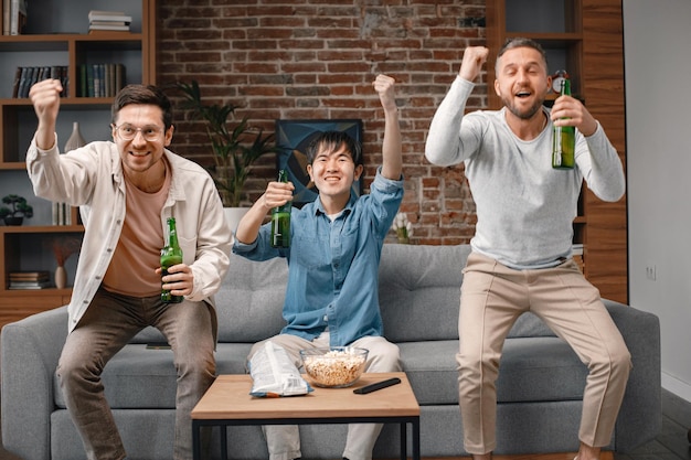 Vista frontal dos homens assistindo a um jogo de futebol na tv e bebendo uma cerveja