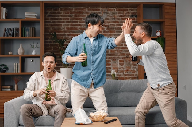 Vista frontal dos homens assistindo a um jogo de futebol na tv e bebendo uma cerveja