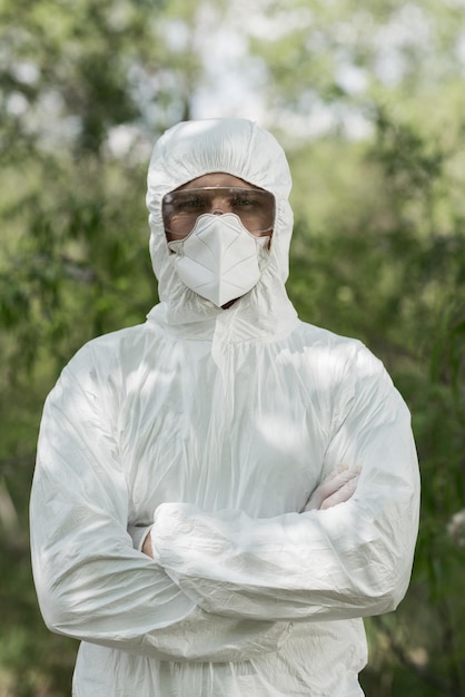 Vista frontal del ecologista en traje protector y respirador con brazos cruzados en el bosque