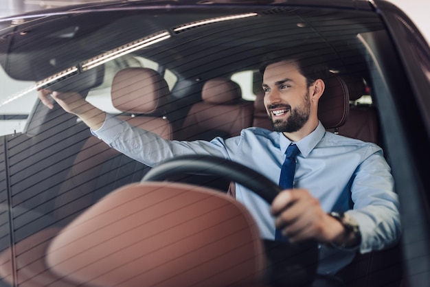 Vista frontal del empresario sonriente ajustando el espejo retrovisor en el coche