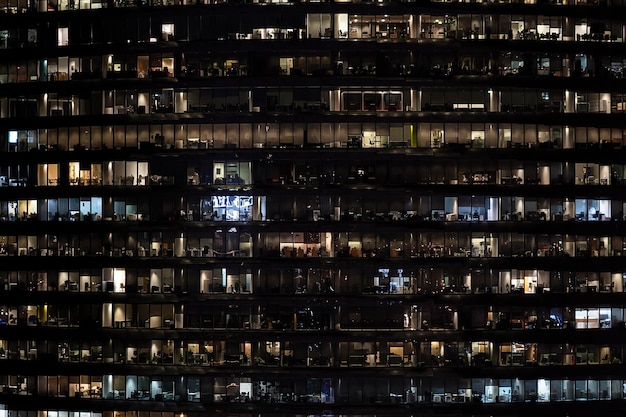 Vista frontal de la fachada nocturna del edificio con muchas ventanas con vida luminosa en cada ventana vista nocturna de la fachada de vidrio de un rascacielos de oficinas