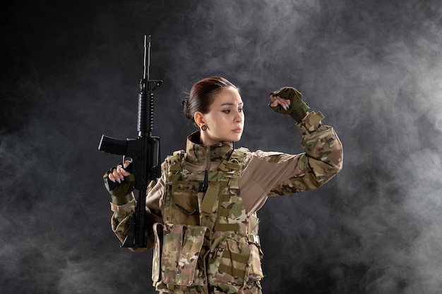 Vista frontal feminina soldado de uniforme com rifle na parede preta