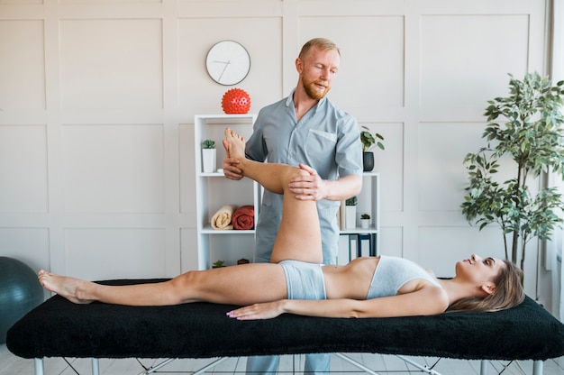 Foto vista frontal del fisioterapeuta masculino realizando ejercicios en paciente femenino