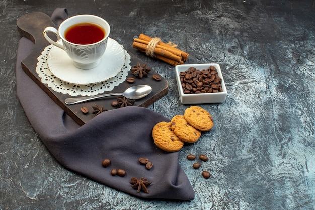 Vista frontal de las galletas caseras canela limones y una taza de té en la tabla de cortar de madera granos de café sobre fondo de hielo