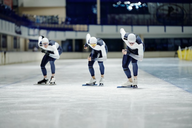 Vista frontal del grupo de jóvenes deportistas que se inclinan hacia adelante mientras patinan de velocidad