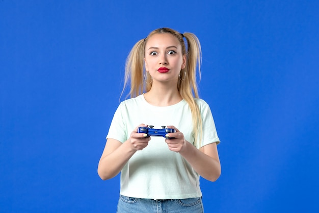 Vista frontal hembra joven con gamepad sobre fondo azul joystick juvenil adulto alegre jugador ganador video virtual
