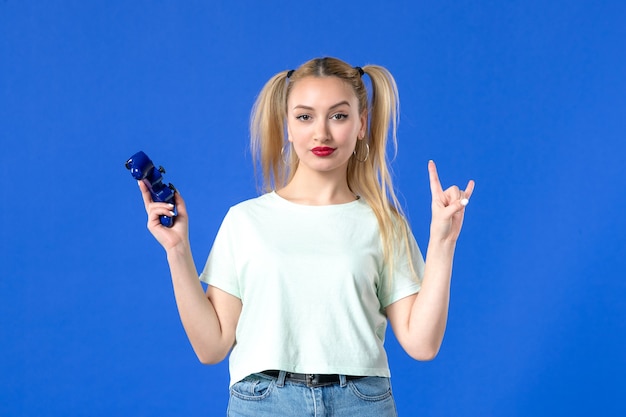 Vista frontal hembra joven con gamepad sobre fondo azul joystick juvenil adulto virtual alegre jugador ganador en línea