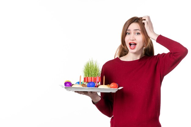 Vista frontal hembra joven sosteniendo honca con semeni y dulces novruz sobre fondo blanco ejecutante étnico vacaciones familiares concepto de colores de primavera