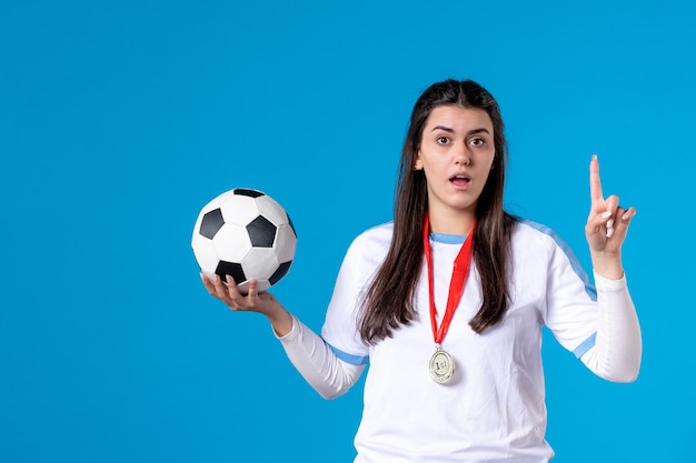 Foto vista frontal de las hembras jóvenes sosteniendo un balón de fútbol en la pared azul