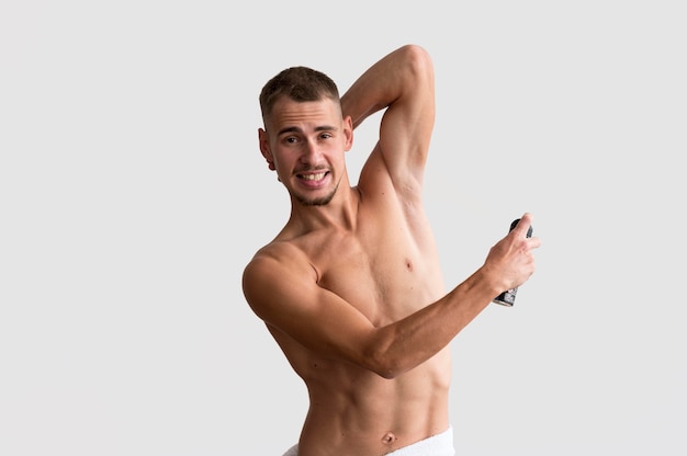Vista frontal del hombre sin camisa aplicando desodorante